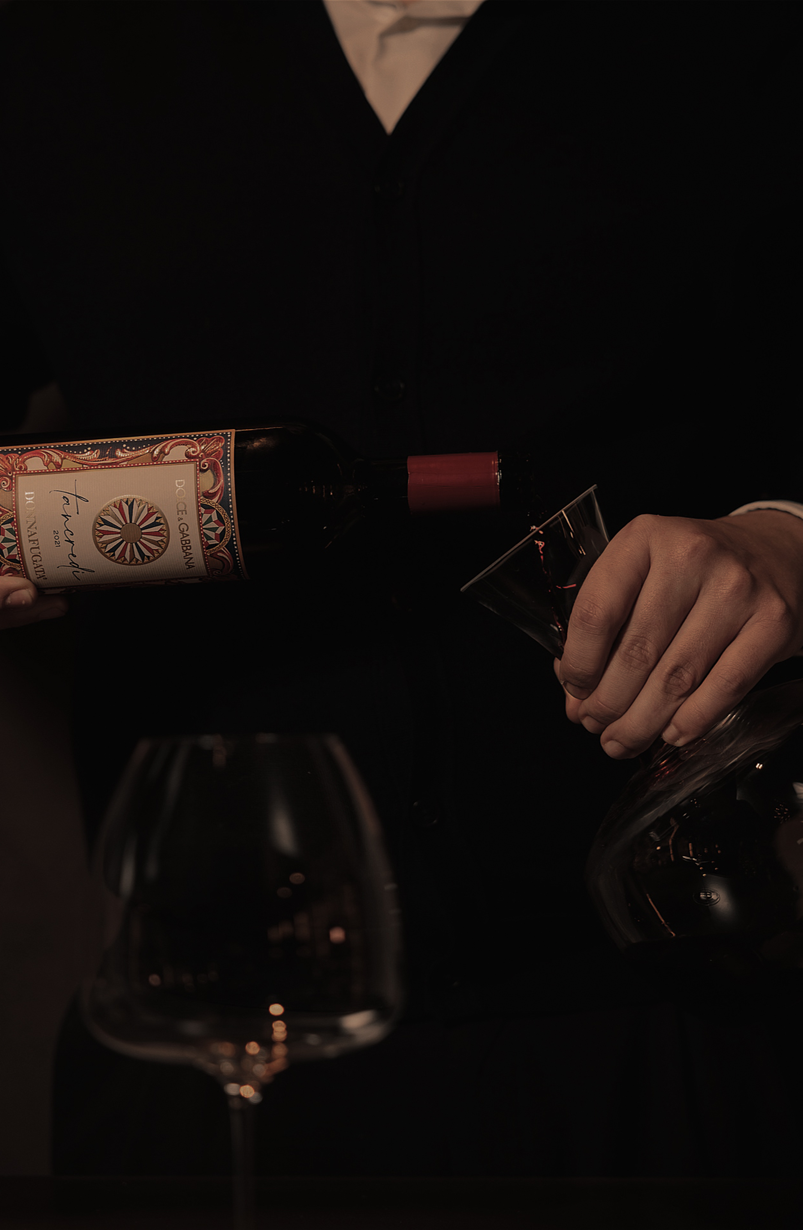 Sommelier versa vino rosso da una bottiglia nel decanter, in un'atmosfera intima e scura